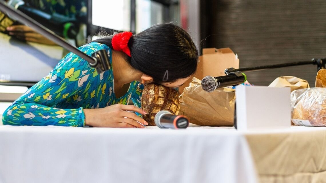 a person making asmr audio by putting their cheek against a loaf of rustic bread