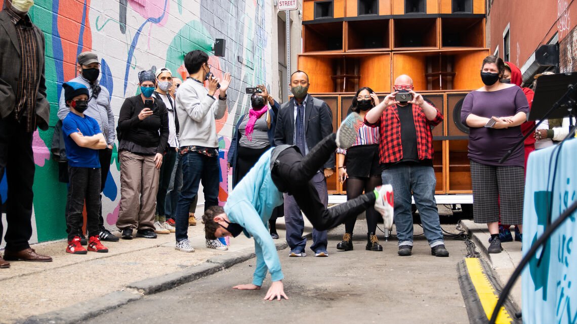 breakdancer in the streets in front of a wall of speaker cabinets and crowd