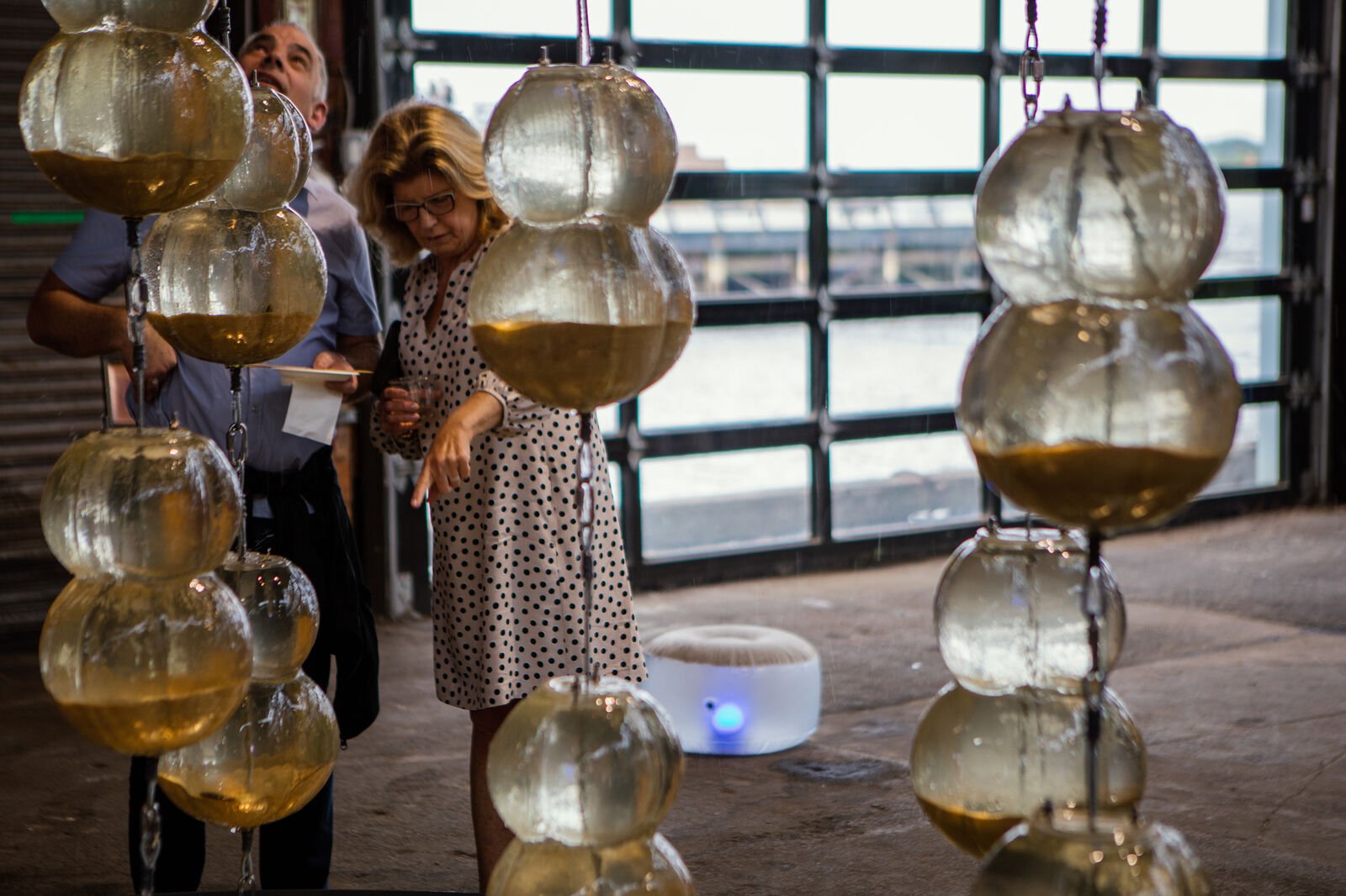 Two guests in the background, pointing at fountain with hanging vessels filled with water, in the foreground
